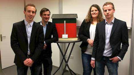 Vier van de vijf studenten die de kadaver afvoertunnel voor etagestallen ontwikkelden. Een schaalmodel van het product staat op de tafel.