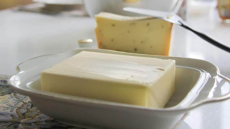 Foto van een botervlootje met verse en boter en kaas op de achtergrond.