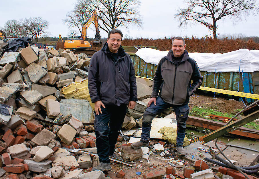 Eric (links) en Twan Stiphout tussen het puin. Ze kijken toe hoe een kraan roosters doormidden knipt.