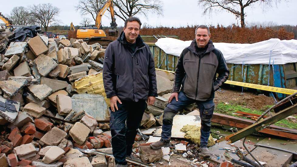 Eric (links) en Twan Stiphout tussen het puin. Ze kijken toe hoe een kraan roosters doormidden knipt.