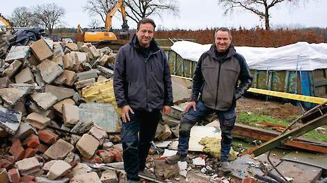Eric (links) en Twan Stiphout tussen het puin. Ze kijken toe hoe een kraan roosters doormidden knipt.