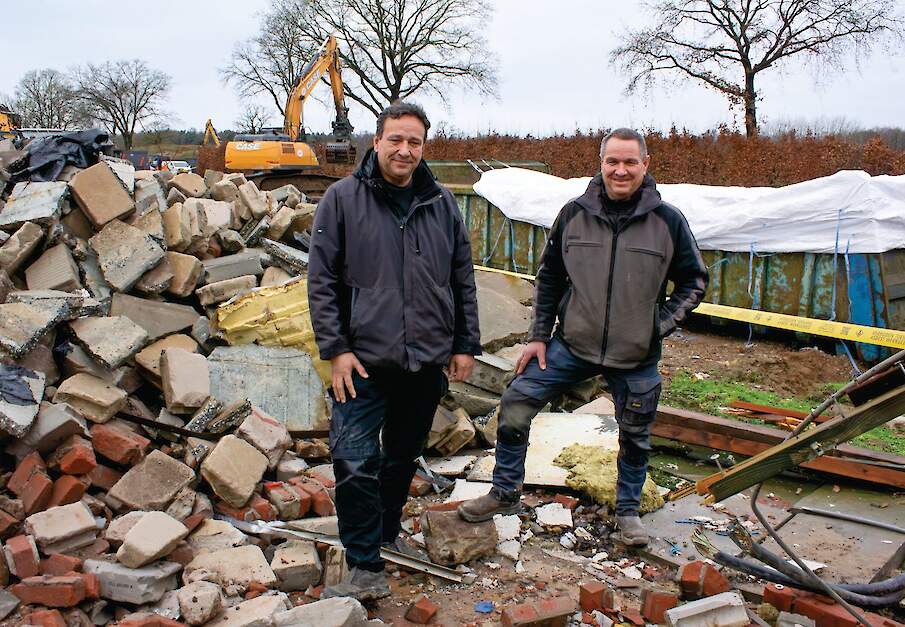 Eric (links) en Twan Stiphout tussen het puin. Ze kijken toe hoe een kraan roosters doormidden knipt.